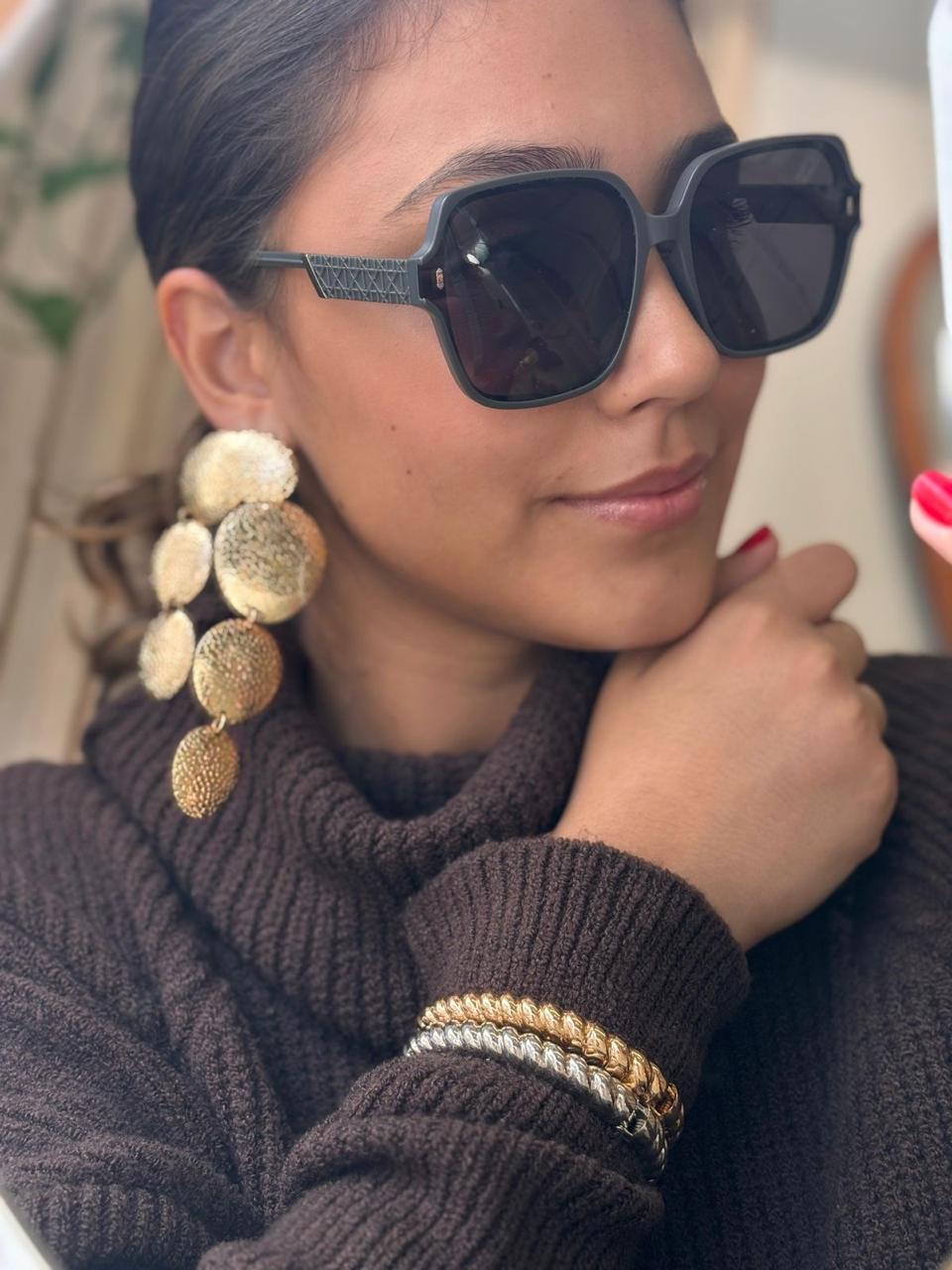 Óculos de sol geométrico preto, brinco longo dourado texturizado e mix de pulseiras metálicas
