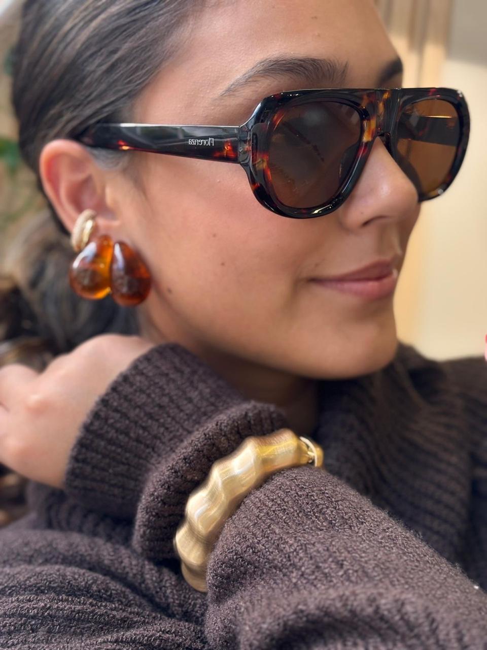 Óculos de sol tartaruga com lentes marrons, brinco em resina âmbar e pulseira dourada ondulada